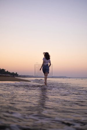Téléchargez les photos : Une joyeuse fille court le long de la mer, attirant les touristes dans les stations balnéaires et les hôtels, soulignant la beauté et la tranquillité du littoral. - en image libre de droit