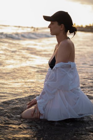 Ein Mädchen sitzt im Morgengrauen am Strand und verkörpert Ruhe und Gelassenheit. Popularisierung von Tourismus, Resorts, gesundem Lebensstil und Outdoor-Sport.