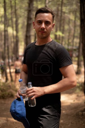 Ein Mann hält eine Wasserflasche in der Hand und löscht seinen Durst beim Wandern im Wald. Ausflüge und Touren, Outdoor-Ausrüstung und Tourismusprodukte, Dienstleistungen von Reisebüros und Öko-Reiseveranstaltern.