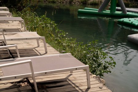 Am Ufer des Sees überblicken Liegestühle einen Gebirgsfluss und aufblasbare Rutschen, die Sommercamping, aktive Freizeit und touristische Aktivitäten bieten.