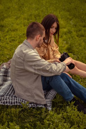 A young couple on a picnic sips hot tea from a thermos, enjoying the convenience and practicality for an active outdoor experience. Refreshments in the open air create a cozy picnic atmosphere.