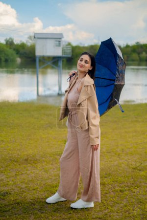 Femme heureuse avec parapluie debout au bord de la rivière, le parapluie offre une protection contre la pluie, rendant les promenades en plein air confortables et sûres.