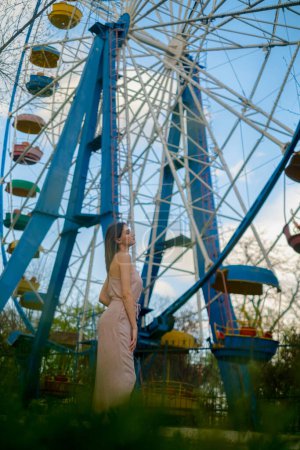 Riesenrad im Vergnügungspark, ein glückliches Mädchen in der Nähe, das die atemberaubende Aussicht genießt, Fahrgeschäft im Vergnügungspark.