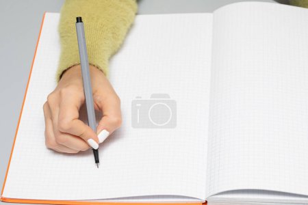 Foto de Mano de mujer que está a punto de escribir en una página vacía de cuaderno con un marcador negro. Amplio espacio de copia y espacio para agregar texto publicitario - Imagen libre de derechos