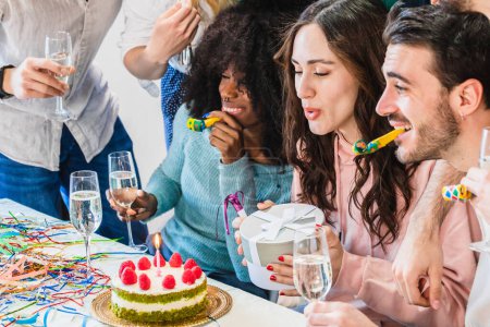 Photo for Birthday party with friends. Girl blowing out candles on cake and holding her present before unwrapping it - Royalty Free Image