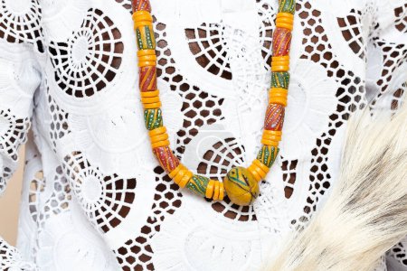 A detailed close-up shot highlighting the intricate design of a traditional African necklace laid on an embroidered white garment, emphasizing the colorful patterns and craftsmanship