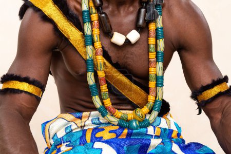 Detail shot of a man in traditional African attire, featuring elaborate handmade jewelry, a golden sash, and fur wristbands, embodying the vibrant and rich cultural fashion