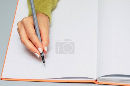 Close-up of a woman's hand writing in a checkered notebook with a gray pen