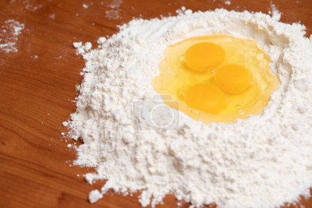 Fresh eggs nestled in a flour well on a wooden surface, ready for mixing into dough