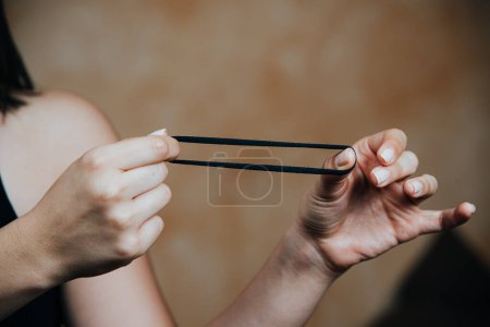 A person's hands manipulating a black hair elastic, a common hair accessory used for styling