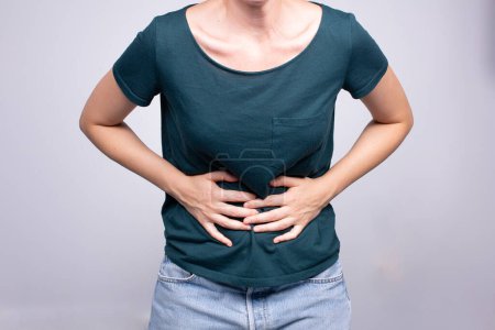 Foto de Una mujer que se agarra el abdomen con molestias, que muestra síntomas que pueden indicar problemas de salud o dolor abdominal - Imagen libre de derechos