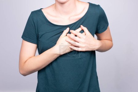 Eine Frau, die sich in Bedrängnis an die Brust fasst, ein Symptom, das häufig mit Angina pectoris assoziiert wird, ein Hinweis auf potenzielle Herzprobleme