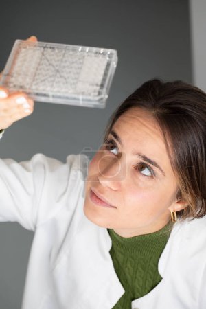Focused female researcher examining a microtiter plate, lab work in progress