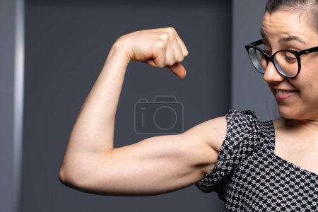 A young woman confidently flexing her biceps, sporting glasses and a joyful smile, symbolizing strength and empowerment