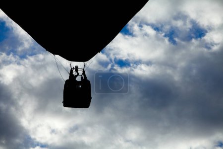 The silhouette of a hot air balloon basket and its passengers stands out against a cloudy sky, encapsulating the thrill of flight