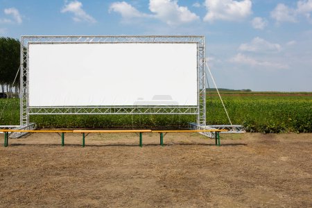 Eine riesige, leere Kinoleinwand steht prominent in ländlicher Umgebung und bietet eine ideale Werbefläche für Vermarkter