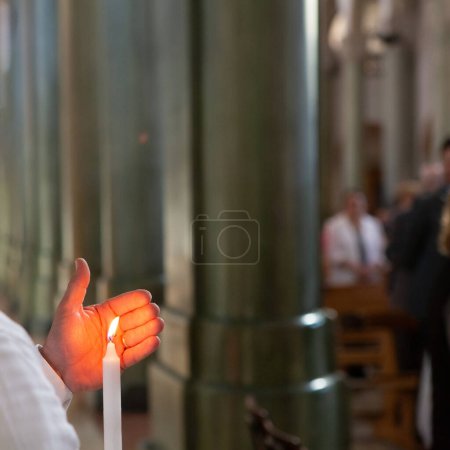 A person's hand holding a lit candle, its flame glowing warmly, during a church ceremony, evoking spirituality and reflection