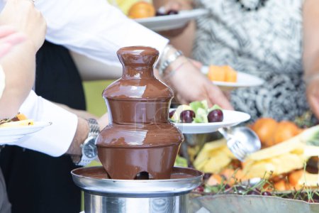a chocolate fountain flows at a social event, where guests serve themselves fruit, creating a sweet centerpiece for the celebration
