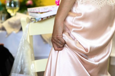 a woman stands elegantly, her hand resting on her pink satin dress with delicate lace details, at a festive event setting