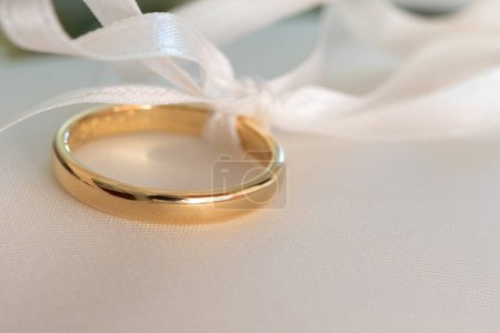 un primer plano de un anillo de bodas de oro delicadamente atado con una cinta blanca, que encarna la promesa de toda una vida