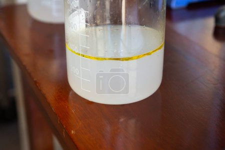 un bécher montre le processus minutieux de distillation des huiles essentielles, capturant une couche d'huile séparée de l'eau, preuve de la précision des méthodes d'extraction