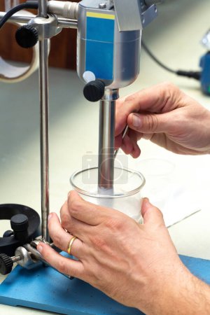 las manos ajustan meticulosamente un agitador de techo en un vaso de precipitados para un experimento científico preciso en un entorno de laboratorio