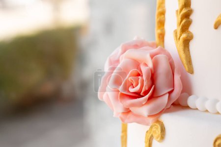 eine wunderschön gearbeitete Fondant-Rose schmückt eine Hochzeitstorte, die durch eine verzierte Goldbesatzung aufgewertet wird und eine luxuriöse Feier verkörpert