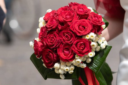 die Braut hält einen atemberaubenden Strauß leuchtend roter Rosen mit weißen Blumen in der Hand, eine klassische Wahl für Hochzeitsfeiern