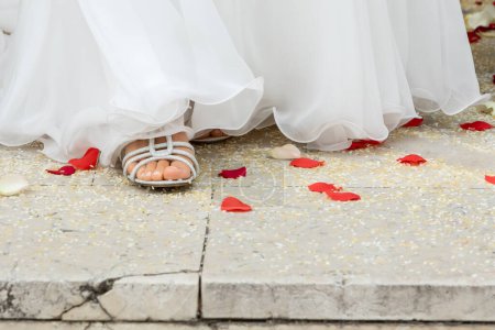 a bride's foot adorned with a chic sandal steps delicately on a romantic trail of rose petals and confetti, marking her walk down the aisle