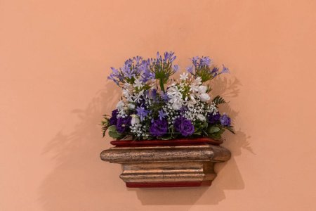 un arreglo floral clásico en un estante de madera adornado, añadiendo encanto a una cálida pared de color melocotón