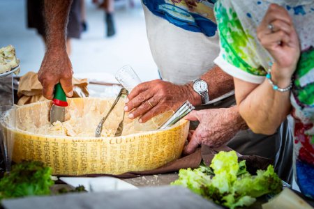 Geschäftiges Markttreiben, bei dem Hände fachmännisch frischen handwerklichen Käse aus einem großen Rad servieren