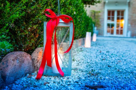 Metalllaterne mit leuchtend rotem Band verleiht einem Gartenweg einen Hauch von Eleganz, wenn die Dämmerung einsetzt