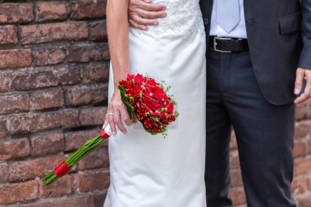 Photo for Close-up of newlyweds' hands clasped, showcasing red floral arrangement. Symbolizes love and partnership - Royalty Free Image
