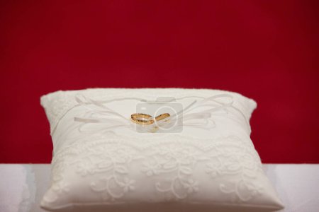 two gleaming golden wedding bands lie on an intricately embroidered pillow, symbolizing eternal love against a vibrant red backdrop