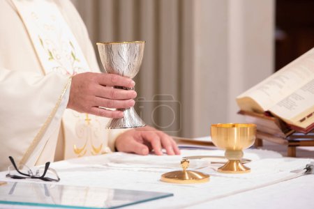 gros plan des mains d'un prêtre tenant un calice décoratif, symbole de foi et de tradition lors d'une cérémonie eucharistique religieuse