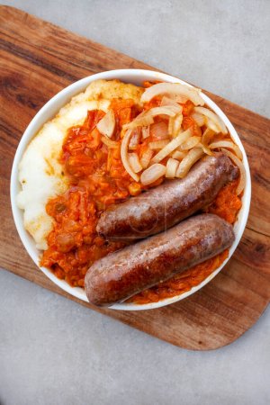 Traditional South African Pap and Wors, sausage with popular maize meal staple covered with Chakalaka or relish on mottled gray with copy space