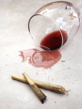 Téléchargez les photos : Marijuana joint avec du vin rouge renversé sur gris - en image libre de droit