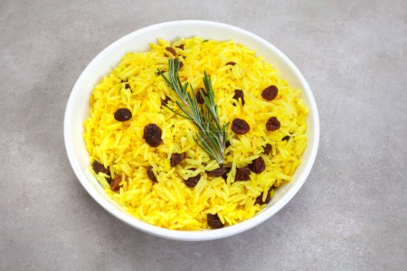 Téléchargez les photos : Riz jaune sud-africain traditionnel, à base de curcuma et de raisins secs avec garniture de romarin, dans un bol rond sur une surface grise tachetée - en image libre de droit