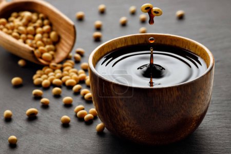 soy sauce drop falling from flying soybeans in wooden bowl and created splash on black stone background. Traditional asian condiment. Natural product concept
