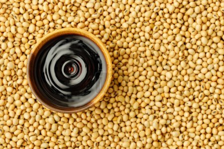 top view of soy sauce falling drop created splash with circle ripple in wooden bowl on dry soybeans as background