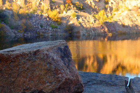 Big stone on the shore of radon lake in former abandoned granite quarry at sunset. Ukraine, Migeia.