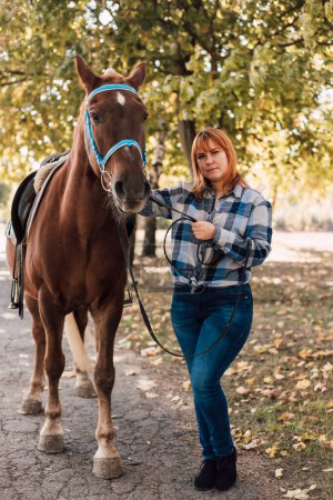 Photo for A woman stands near a horse. Farming, horseback riding. Autumn Park. High quality photo - Royalty Free Image