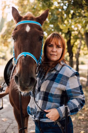 Photo for A woman stands near a horse. Farming, horseback riding. Autumn Park. High quality photo - Royalty Free Image