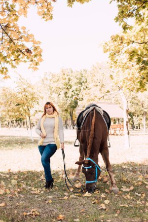 Photo for A young woman in a shirt stands next to a brown horse. Horseback riding in the autumn forest. High quality photo - Royalty Free Image