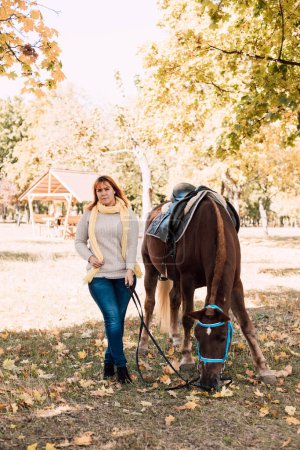 Photo for A young woman in a shirt stands next to a brown horse. Horseback riding in the autumn forest. High quality photo - Royalty Free Image