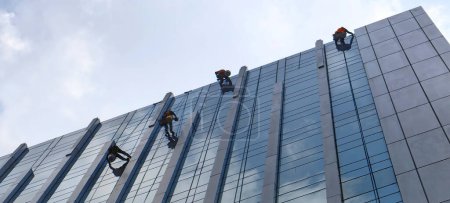 Photo for Employee cleaning the glass of a high-rise building city office Abseiling from the roof of a building - Royalty Free Image