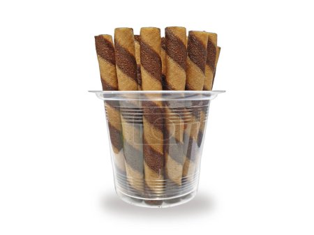 Group of chocolate wafer rolls in a clear plastic bowl isolated on white background. Delicious snack of rolled waffles filled with chocolate, it tastes sweet and crispy. Choco sticks rolls topping.