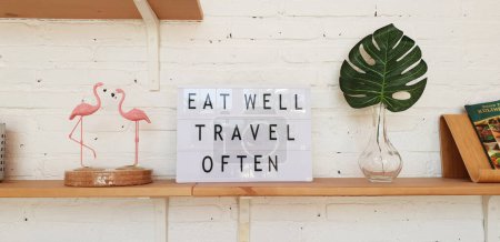 Home interior of a trendy, stylish, bright Scandinavian-style kitchen with open shelves. Minimal cozy kitchen with white brick wall, bright wooden shelf and letter board quote EAT WELL TRAVEL OFTEN.