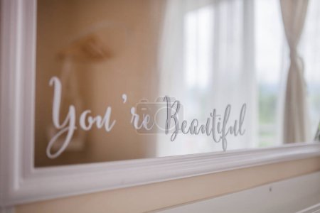 You are beautiful mirror cutting sticker with blurred background of the room and window. Typography quote of self love, self care, self appreciation. Positive, health, beauty and wellness concept.
