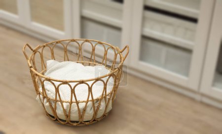 Rattan wicker basket with white natural cushion inside. Selective focus with dressing room decor blurred background. Fashionable storage basket stylish interior item eco design handmade.